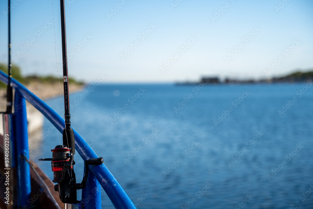 A backlit closeup picture of a blue rail and a fishing rod on a boat. Clear blue sky and ocean in the background A backlit closeup picture of a blue rail and a fishing rod on a boat. Clear blue sky and ocean in the background