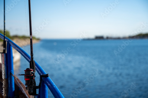 A backlit closeup picture of a blue rail and a fishing rod on a boat. Clear blue sky and ocean in the background