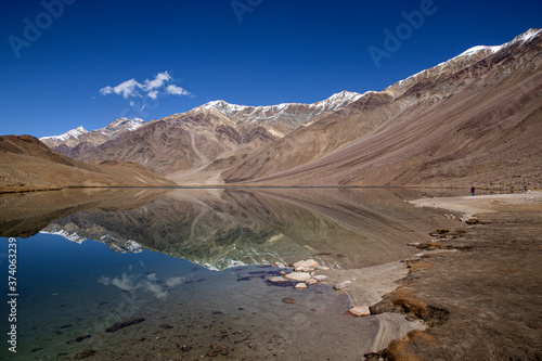 Tourist enjoy the serene view of Chandra Tal on a clear day with beautiful reflection of hills and clouds on the lake