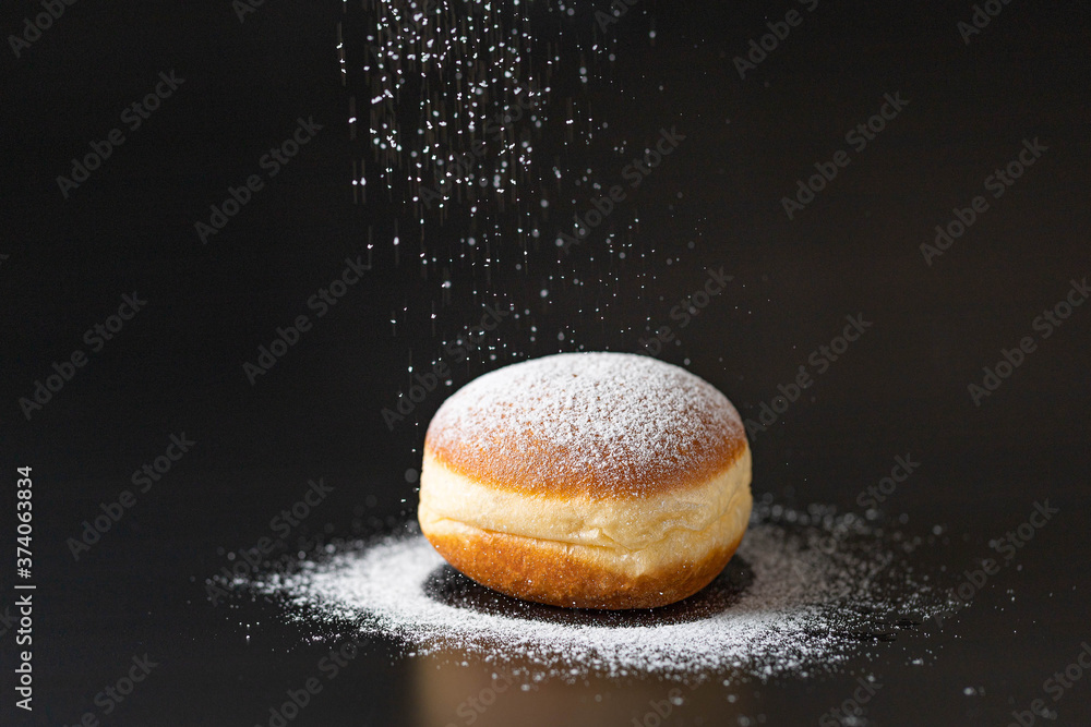 doughnut with powdered sugar infront of a black background - obrazy, fototapety, plakaty 