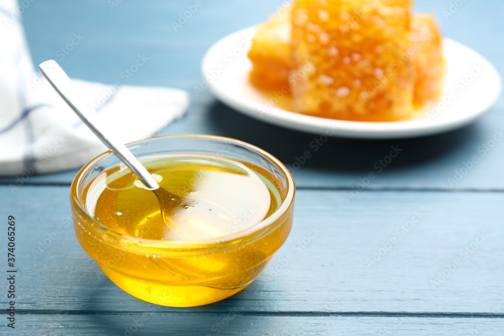 Fresh honey in bowl on blue wooden table, space for text