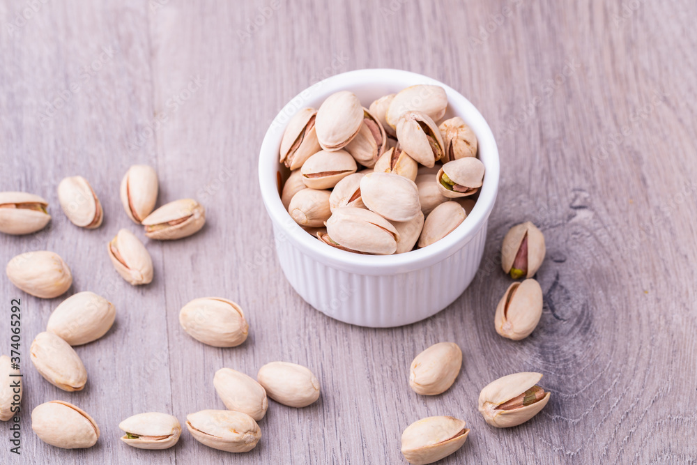 Pistachio nuts in a white ceramic bowl on a wooden table. Pistachio nuts in a white ceramic bowl on a wooden table.