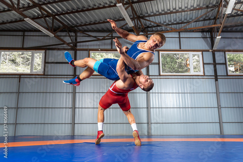 The concept of fair wrestling. Two greco-roman wrestlers in red and blue uniform making a suplex wrestling on a wrestling carpet in the gym.The concept of male wrestling and resistance