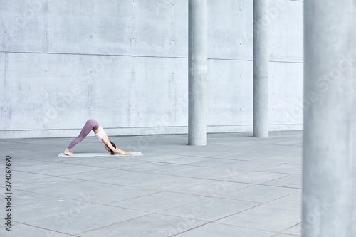 Frau/Mädchen in Pastell gekleidet macht Outdoor Yoga Übungen/Sonnegruß in moderner Beton Architektur. Urbanes Leben. 