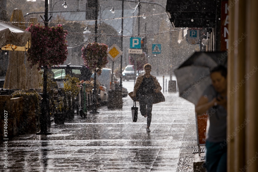 Ulica w deszczu i zmoknięty człowiek biegnący chodnikiem. - obrazy, fototapety, plakaty 