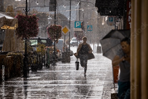 Ulica w deszczu i zmoknięty człowiek biegnący chodnikiem.