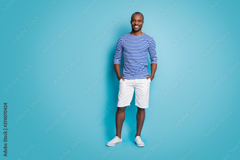 Full body photo of positive cheerful satisfied afro american guy enjoy rest relax put hands pocket wear trendy clothes gumshoes isolated over blue color background Full body photo of positive cheerful satisfied afro american guy enjoy rest relax put hands pocket wear trendy clothes gumshoes isolated over blue color background