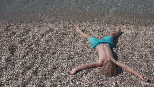 Child enjoy summer vacation on the seaside. Smiling boy lying and relaxing on beach alone. Tourism, resort, healthy lifestyle, happy childhood concept
