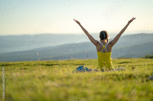 Slim and attractive Caucasian woman with her hands raised to the sky in a yoga session in nature on a sunny summer day. The joy and pleasure of recreational activities in nature. Copy space.