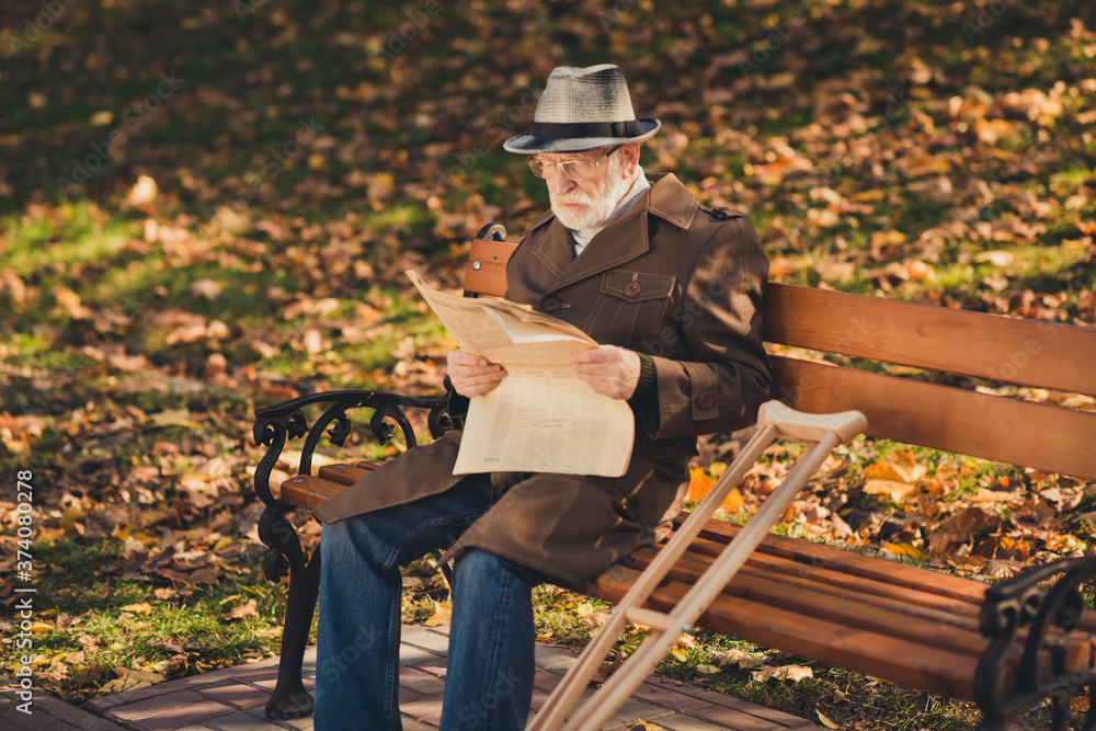 Profile side photo of serious lonely old man rest relax in autumn leaves grass lawn park sit bench crunch read newspaper attentive wear season outerwear Profile side photo of serious lonely old man rest relax in autumn leaves grass lawn park sit bench crunch read newspaper attentive wear season outerwear