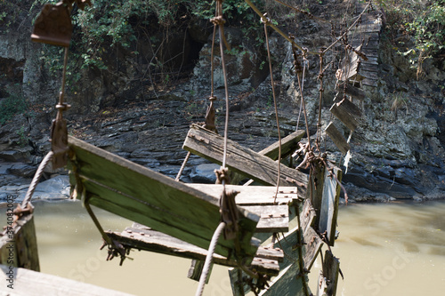 Broken bridge made from wood and steel rope over a mountain river.
