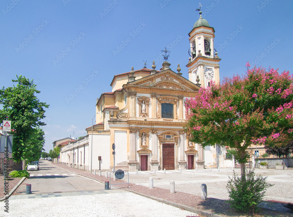 Baroque facade in white and gold of a church seen from the large churchyard with flowering trees