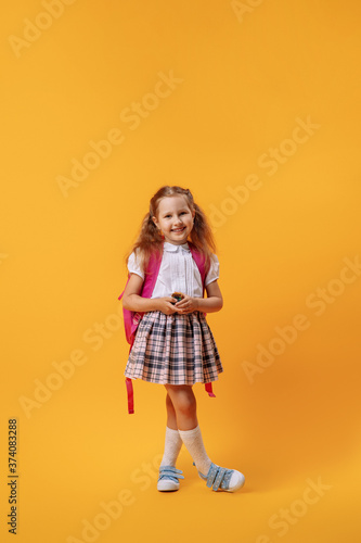 happy smiling little girl in a uniform with a backpack and a toy in her hands