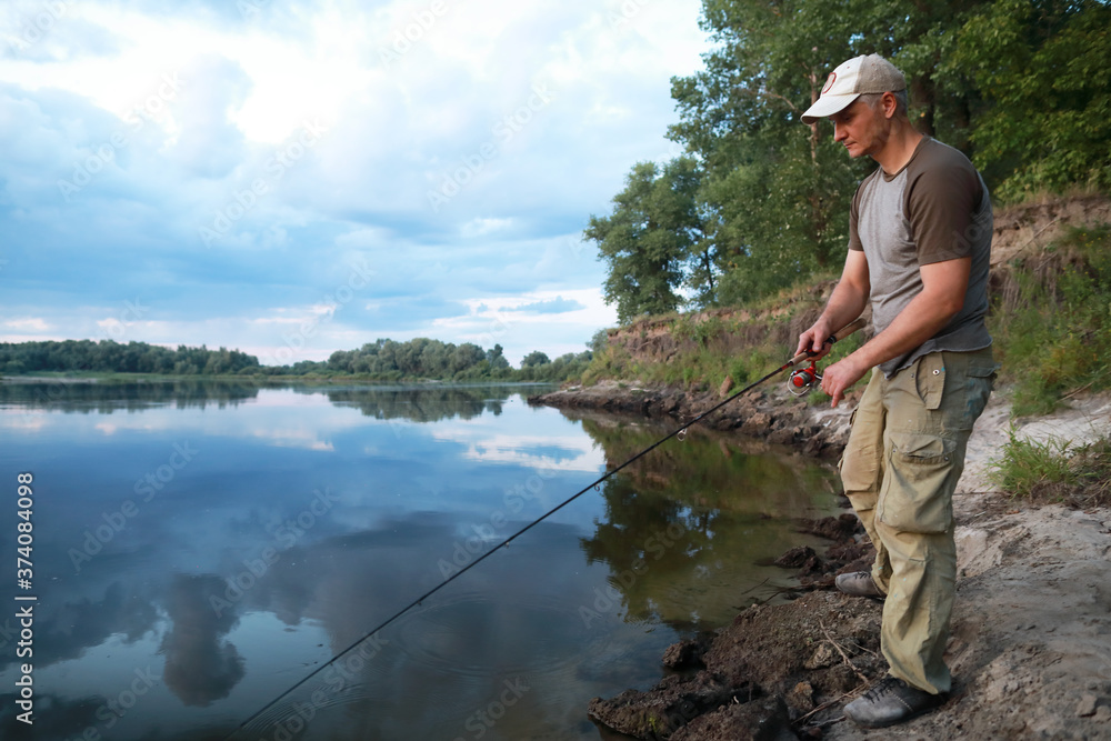 Caucasian adult man fishing in evening with beautiful reflection sky and clouds on the river. Caucasian adult man fishing in evening with beautiful reflection sky and clouds on the river.
