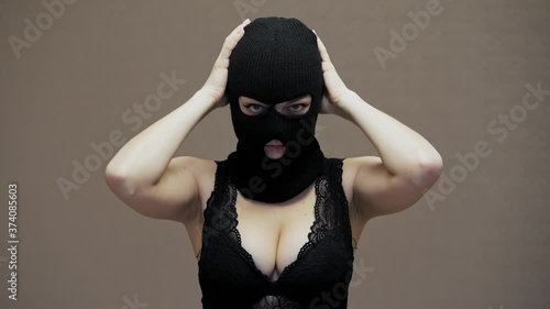 Sexy woman puts on hacker black balaclava mask, dressed in lace bra, robbery concept