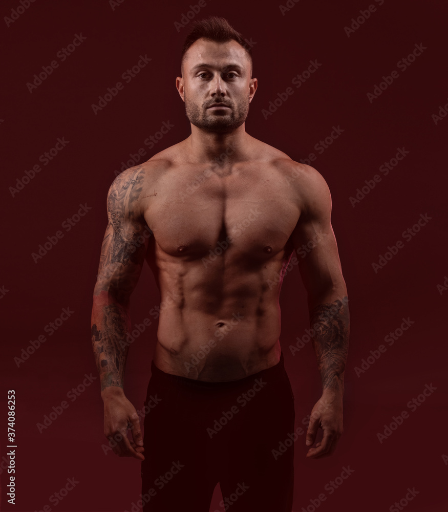 Bodybuilder strong man with an ideal body on red dark background.