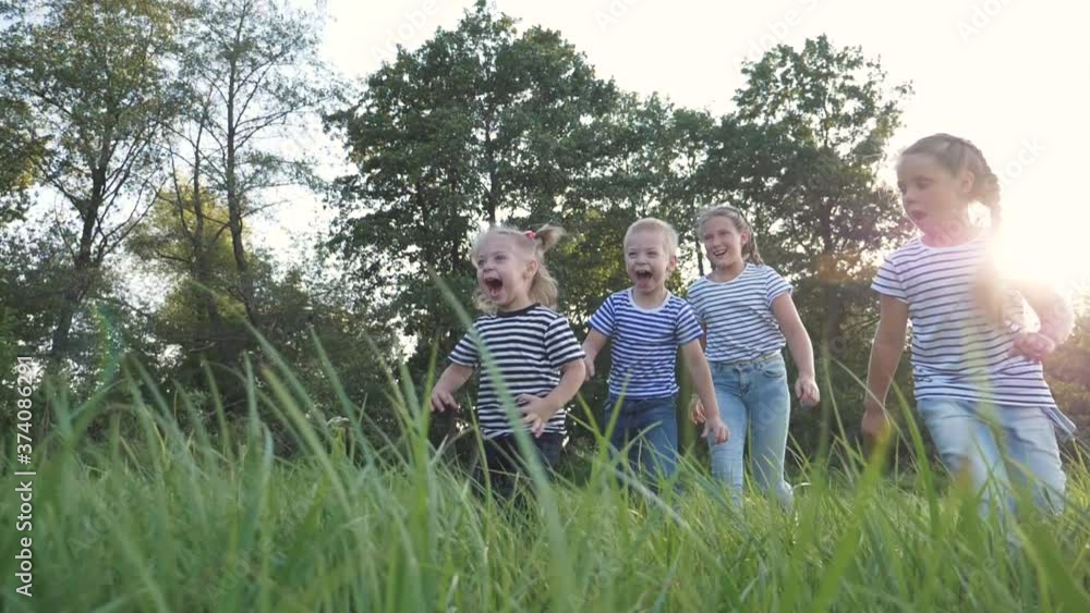 Happy family of children has fun in the park. Children flee the green lawn in droves. Kids play fun at sunset in the park. Teamwork, playing girls and a boy. Happy family of children has fun in the park. Children flee the green lawn in droves. Kids play fun at sunset in the park. Teamwork, playing girls and a boy.
