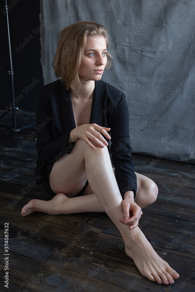portrait of young caucasian woman with short hair in black suit jacket, sitting on floor in front of fabric background. model tests of pretty girl. short-haired attractive female poses in studio