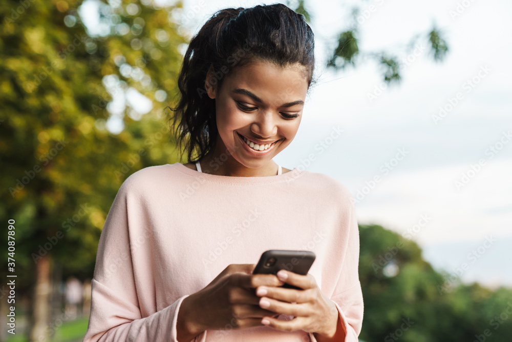 Image of african american girl using mobile phone while walking in park Image of african american girl using mobile phone while walking in park