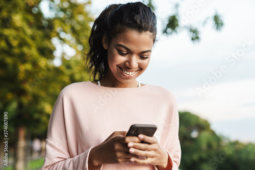 Image of african american girl using mobile phone while walking in park