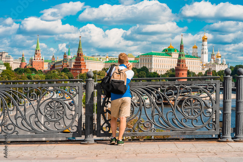 Canvas Print A young blond man stands on a bridge and admires the Kremlin and the river in Mo