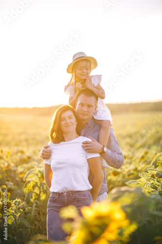 Father  mother and little daughter in straw hat in sunflowers field on sunset.