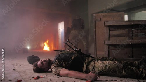 Brave military man evacuating seriously wounded in head fighter from battlefield, pulling by belts of body armor. Warrior helping injured soldier, dragging unconscious friend from area under fire