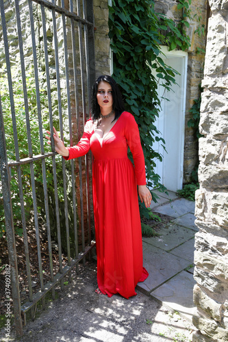 Woman in long red gown pushes open wrought iron gate to escape from the castle