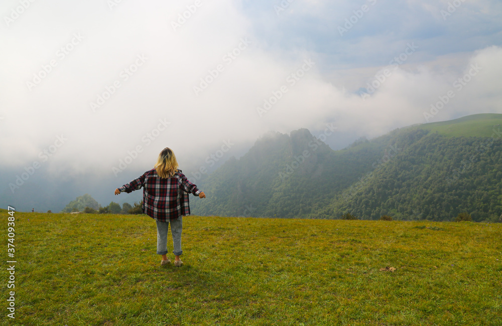 Woman traveller with stretched arms standing at the top of the hill in Caucasus mountains Russia. Happy girl hiker in the mountains.