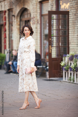 Beautiful smiling middle age woman in the dress walking at the city street on a sunny day.