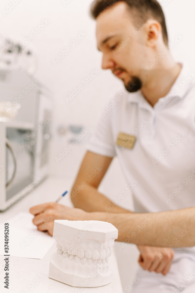 The concept of writing to the dentist. The man writes something on the patient's medical record. In the foreground is an artificial jaw The concept of writing to the dentist. The man writes something on the patient's medical record. In the foreground is an artificial jaw