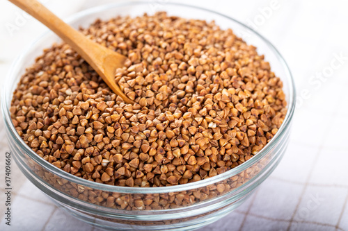 Bowl of raw buckwheat with spoon on wooden background. Buckwheat groats (hulled seeds) in bowl.