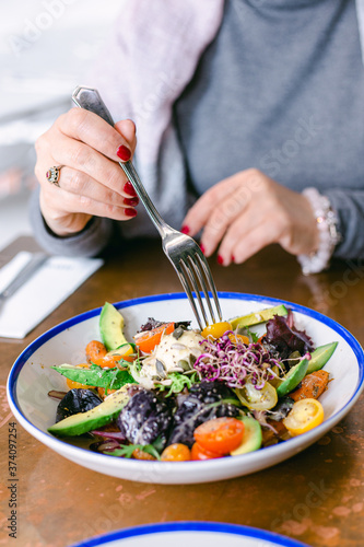 Fototapeta Naklejka Na Ścianę i Meble -  Happy woman eating healthy salad with tomatos cherry,  greens, avocado and carrots. Woman wearing grey jersey is eating business lunch