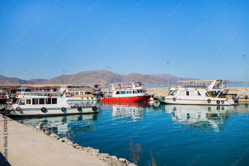 Tourist boats in bay near Akdamar island on Van Lake, Gevaş, Turkey. Bright blue colour of water is created by saline soda elements in its consist. Monastery on island is popular tourist destination