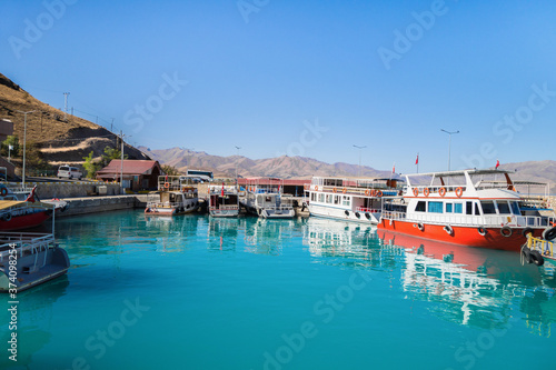 Bay with tourist boats near Akdamar island on Van Lake, Gevaş, Turkey. Lake & island are popular tourist destinations. Bright blue color of lake water is created by saline soda elements in its consist