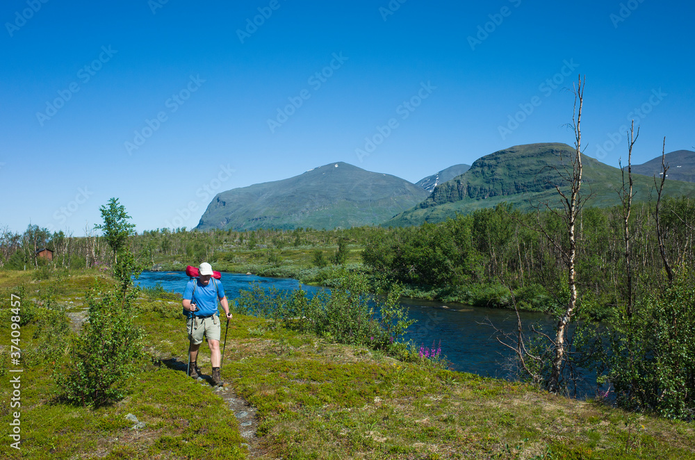 Hiking in Sweden in summer. Man tourist trekking in Abisko National Park in northern Sweden. Nature of Scandinavia in sunny day blue sky