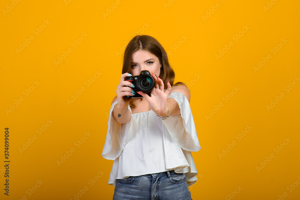 Young female photographer with camera over yellow background