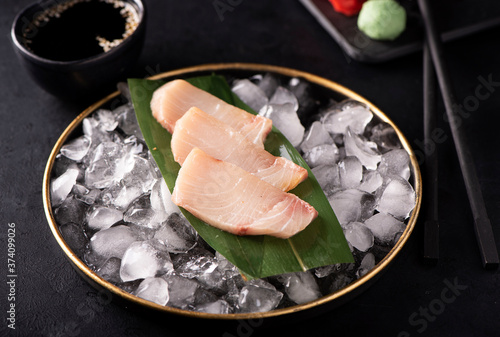 yellowtail sashimi on ice in a black plate