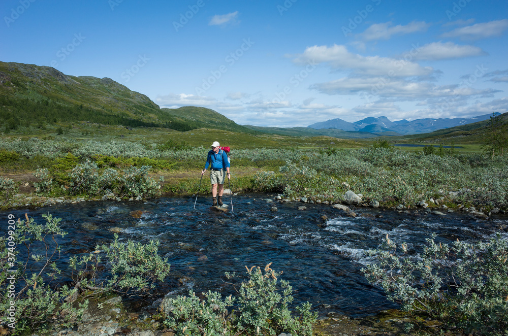 Hiking in Swedish Lapland. Man crossing river, Trekking  in Sweden in summer. Arctic nature of Scandinavia in warm sunny day