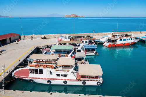 Tourist boats in bay on Van Lake, near Gevaş, Turkey. Akdamar island with Cathedral of Holy Cross are on background. It's popular tourist destination among foreign & local travelers photo