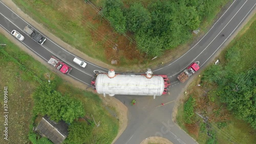 A truck driver with an oversized cargo on a trailer makes a turn on a narrow road followed by a traffic inspection vehicle. Delivery and logistics of goods from different places, top view
