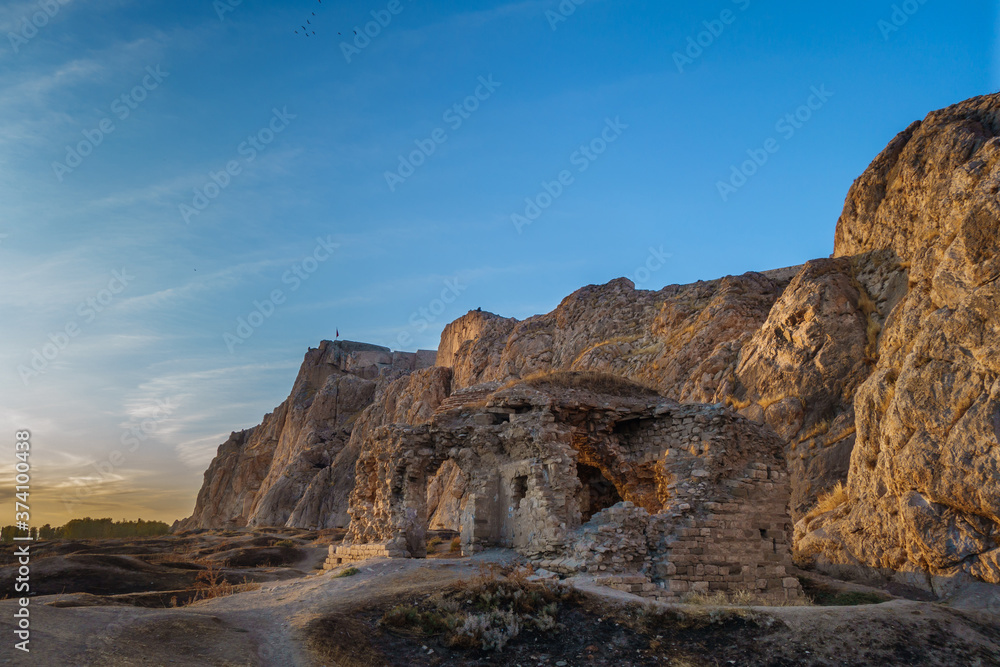 Evening view onto ruins of building (mosque or church) in Old City of Van, Van, Turkey. Van Rock with its famous fortress is on background. Rock & ruins are painted with golden light of sunset