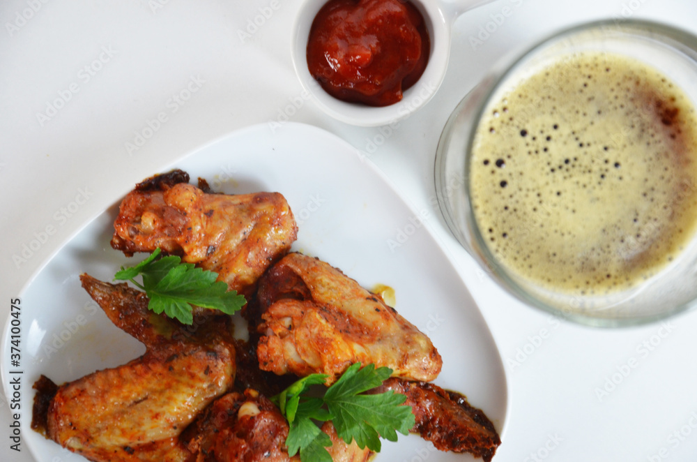buffalo chicken wings barbecue or grill with red sauce in a gravy boat, beer in a tall glass with foam on a white background buffalo chicken wings barbecue or grill with red sauce in a gravy boat, beer in a tall glass with foam on a white background