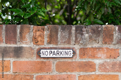 Country No Parking sign on brick wall with green leaves behind