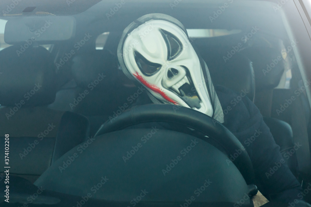 Halloween. Man in a terrible mask in a car in the driver's seat harvests pumpkins and scares.