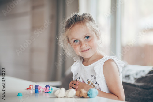 Little cute preschooler child girl playing educational games with plasticine figures preparing for school in kindergarten while sitting at table. Back to school concept.