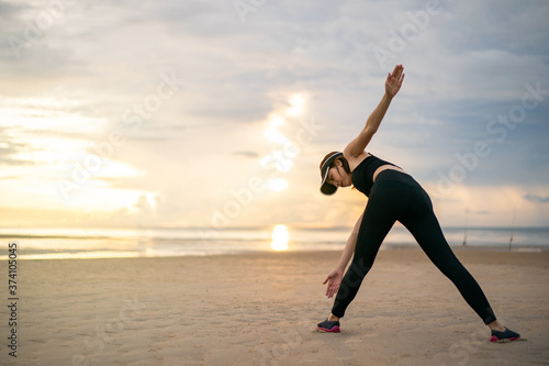 Woman doing exercise with cross body toe touches for back Stretch on the beach with sunrise on the morning.