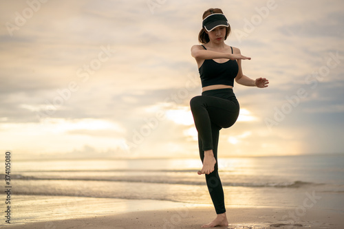 Woman doing high knee twist exercise on the beach with sunrise on the morning.