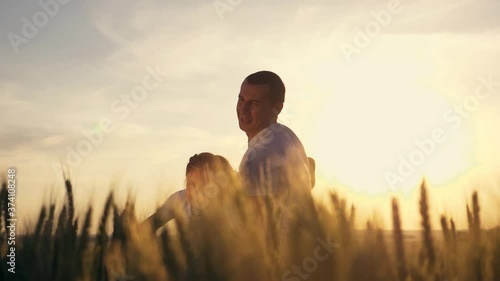 Happy family. A parent is circling, rocking a little girl in the Park at sunset in a large wheat field. The child in the hands of the father as the plane flies, playing the pilot.