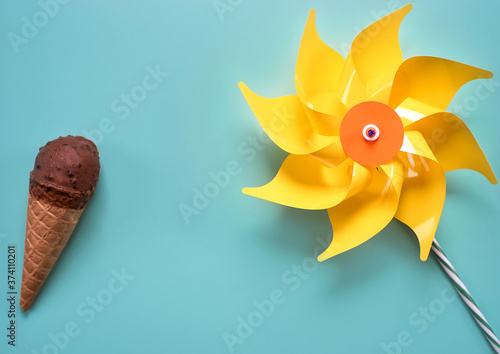 Bright yellow windbreaker toy and ice cream in a horn with chocolate glaze on an isolated blue background. Summer mood.
